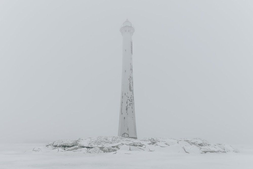 Foggy lighthouse in a calm and desolate winter landscape. A white old lighthouse isolated in mist.