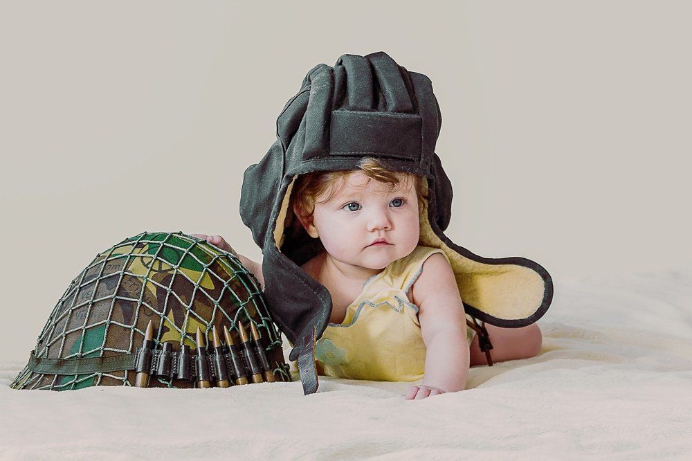 Маленький ребенок в шлеме танкиста и с военной каской.