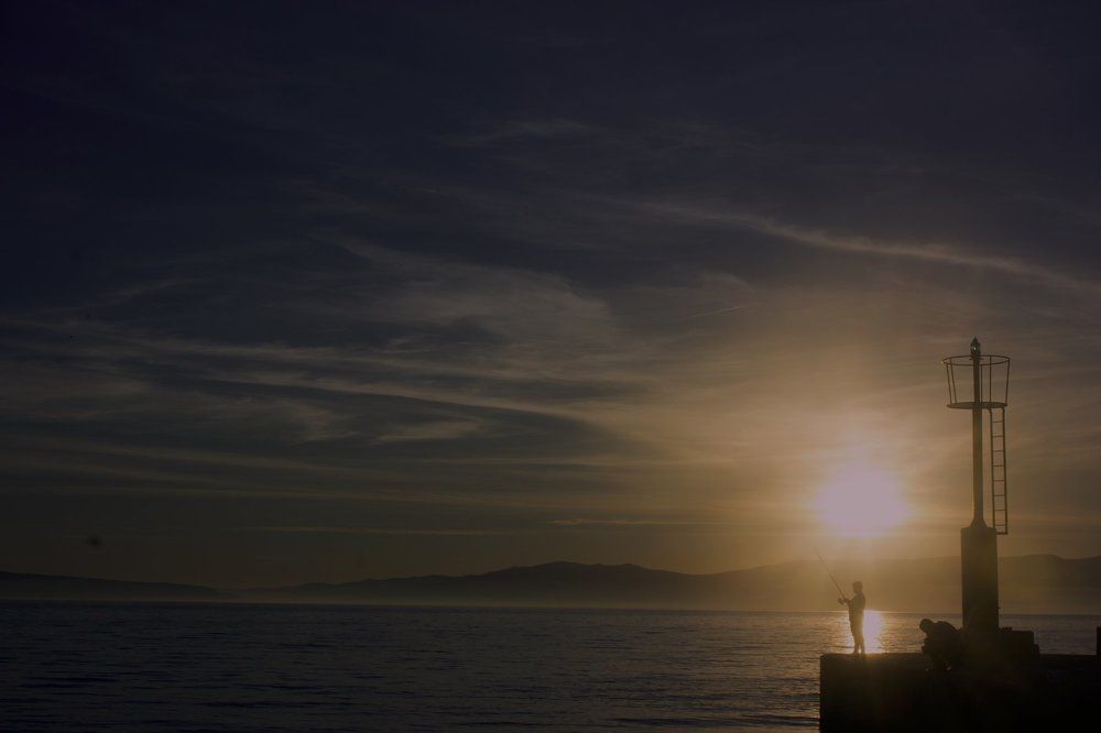 Little boy is fishing at sunset