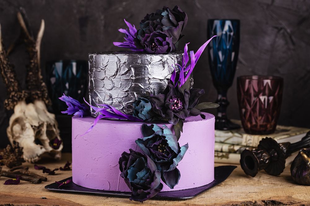 Tiered cake with black flowers on dark background with halloween decorations