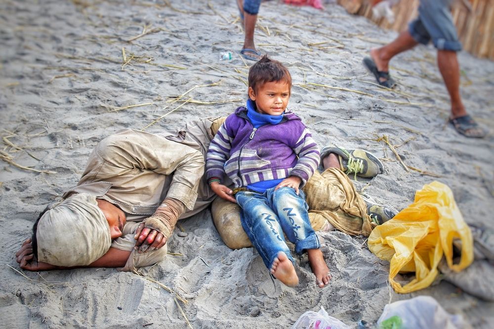 A leprous man lying on the ground beside the road at beach to begging with his little son
