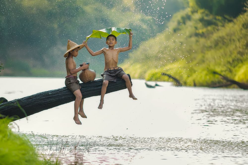 Little boy playing with friend in the river at countryside, rainy or autumn day.