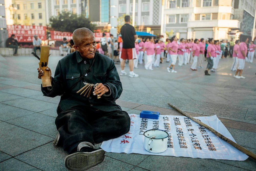 Слепой  старик просит милостыню на фоне танцующих жителей