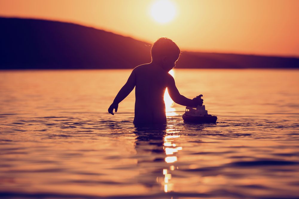 Boy is playing with a boat on sunset