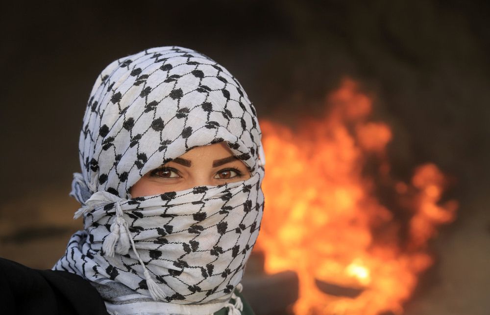 A Palestinian woman shouts slogans as other Palestinians burn tires in response to Israeli interventions during a "Great March of Return" demonstration on the Israel-Gaza border in Gaza City, Gaza .