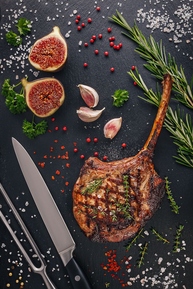 Pork chop tomahawk on slate board with figs and herbs