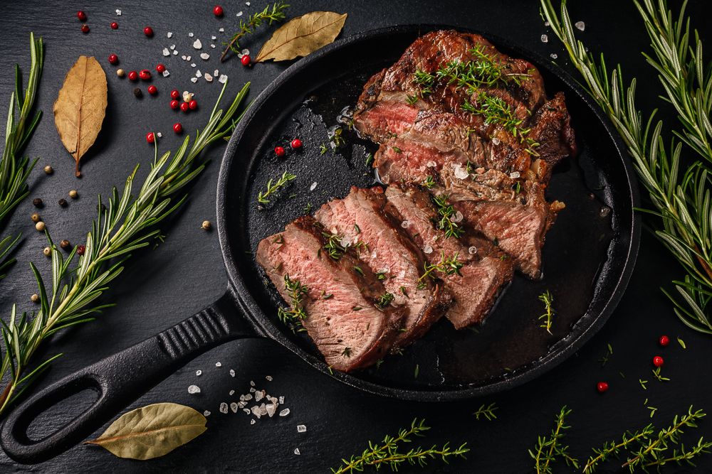 Sliced beef steak in a cast iron pan on slate board.