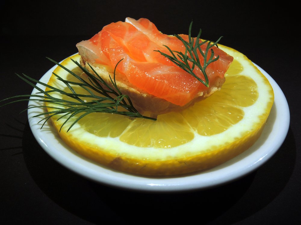 Бутерброд с семгой и лимоном на белой тарелке.