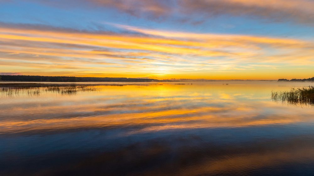 View of the lake during the sunrise, bright, colorful sky, reflected in the water.