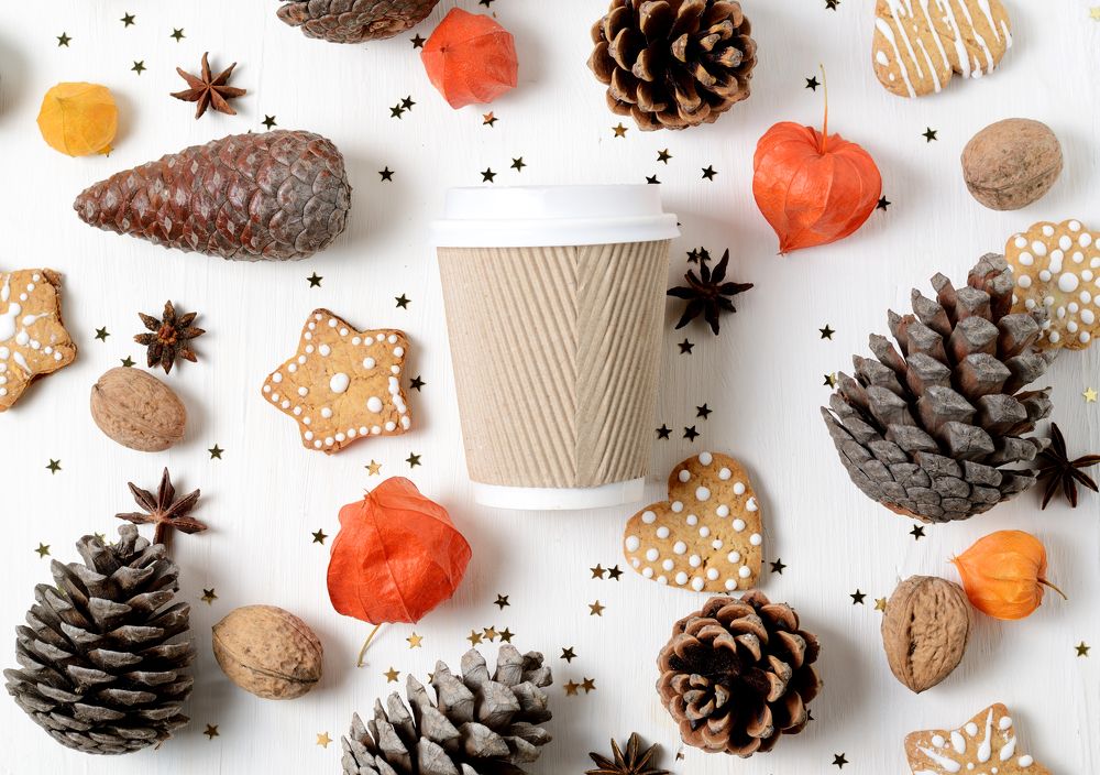 Takeaway paper coffee cup among cookies, pine cones and other christmas decor.