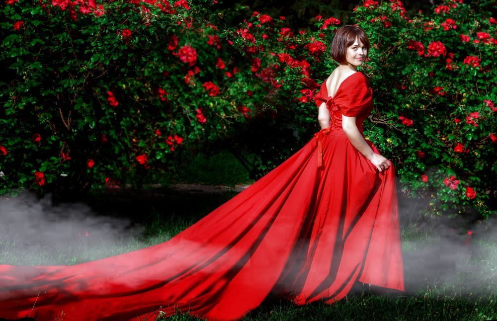 A girl in a long red dress in a blooming rose garden