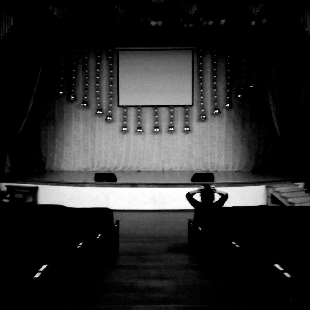 Одинокая женщина в кинотеатре поправляет причёску.