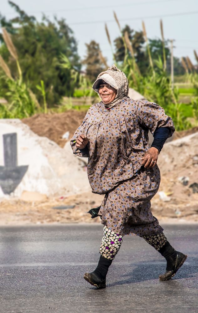 An Egyptian rural woman crosses the road and smiles