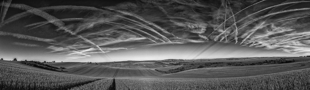 Wavy fairytale spring landscape with fields and contrails chemtrails on the sky