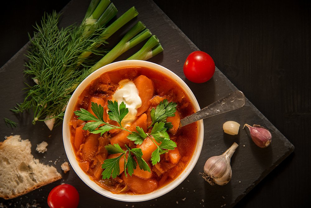 Borscht soup, bread and vegetables on a table of dark wood.