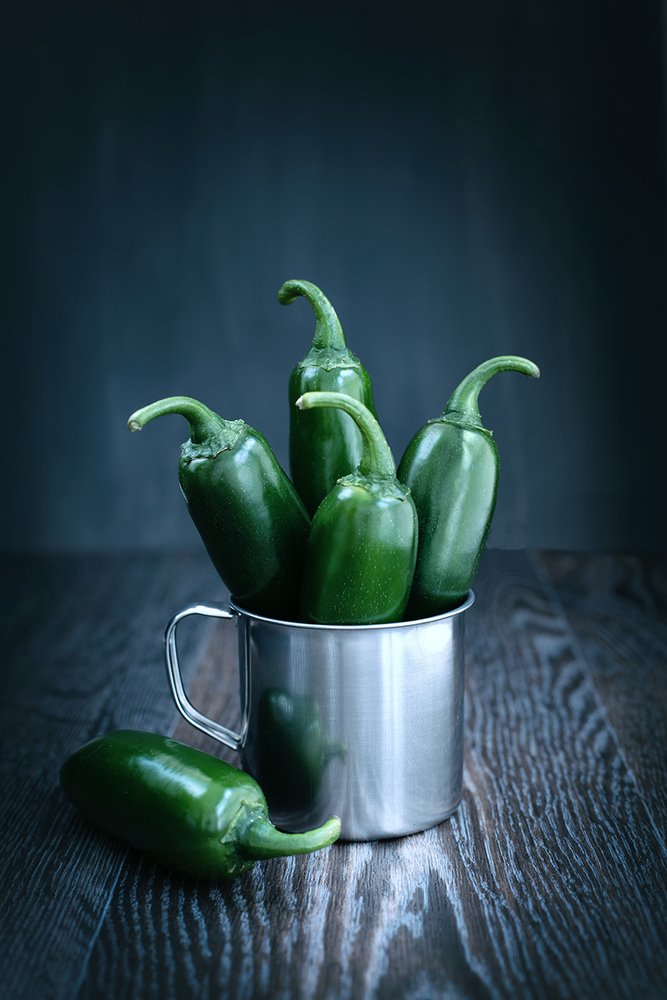 Green pepper in a metal mug on a wooden table in the moonlight.