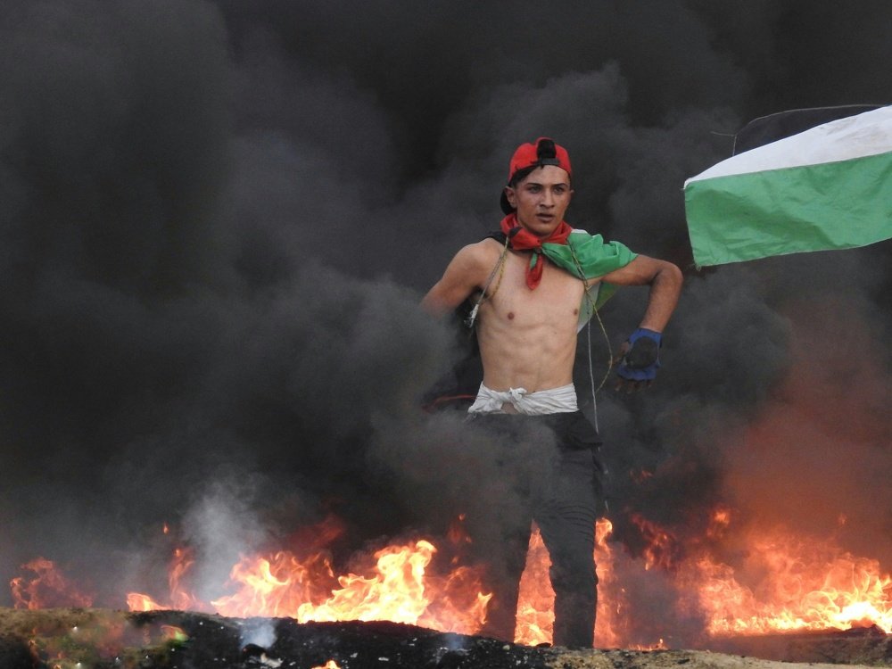 A Palestinian youth burn tires to cover them and avoid being targeted by Israeli snipers during the return marches and breaking the siege east of Gaza .