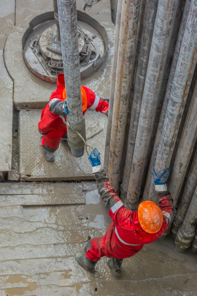 Два рабочих буровика устанавливают поднятую из скважины бурильную трубу.