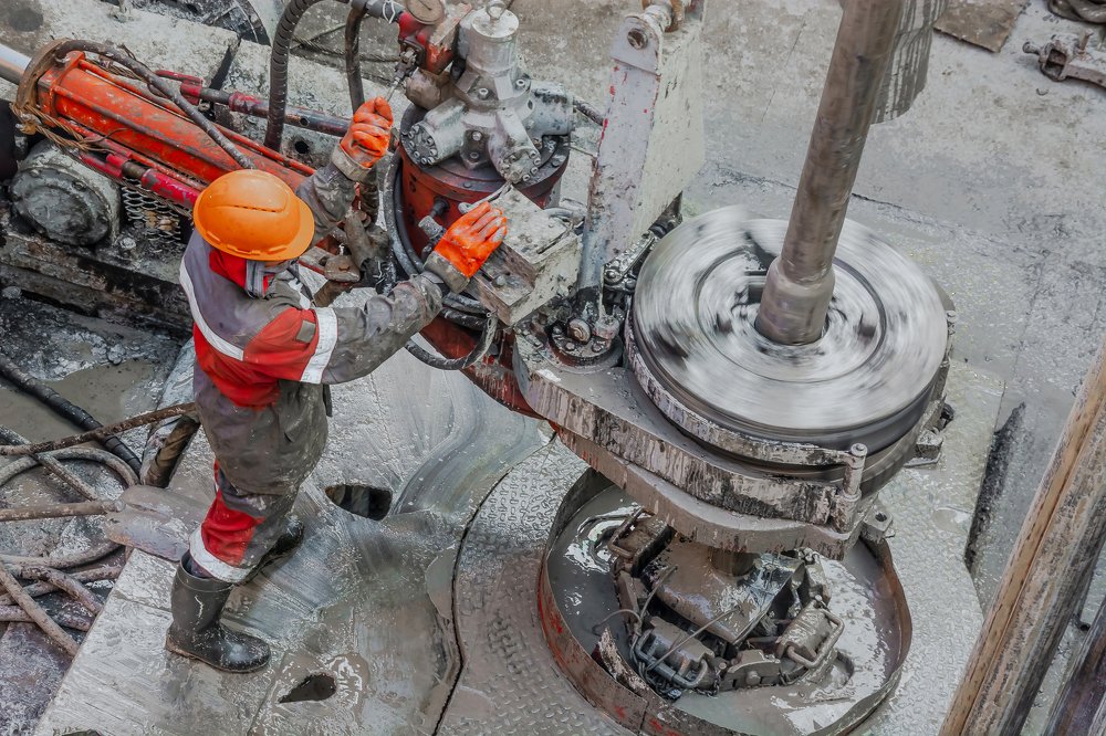 Рабочий буровик свинчивает бурильные трубы для спуска в скважину.