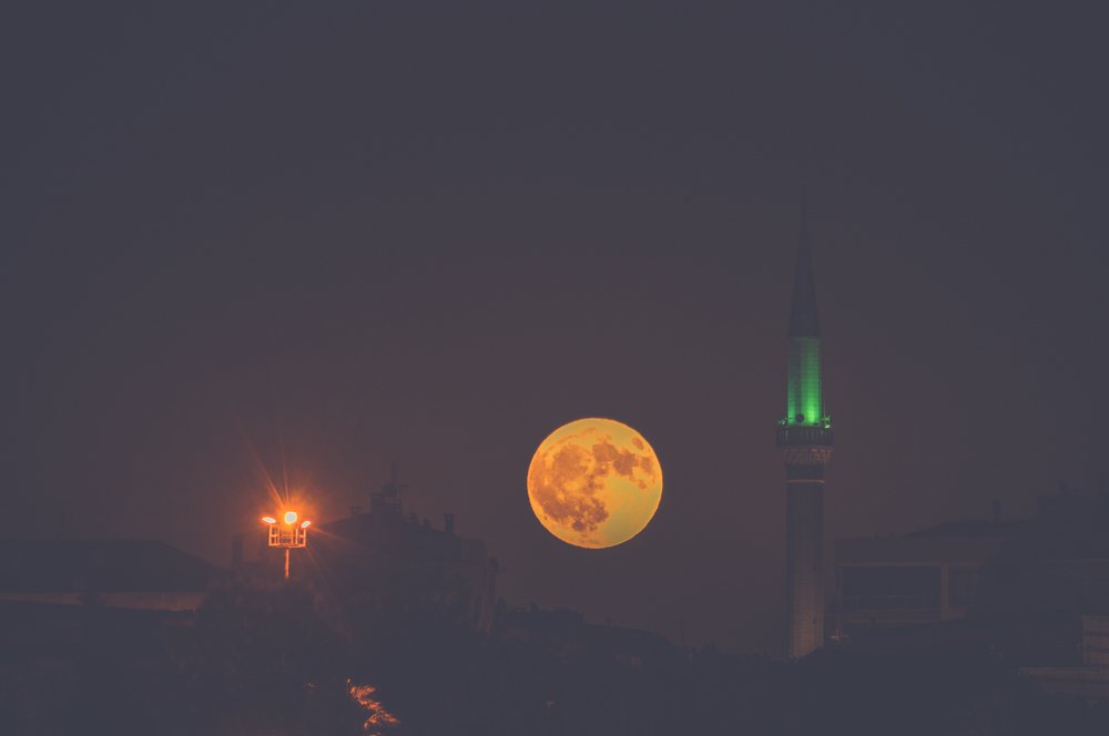 Dramatic full moon rising over at night with mosque silhouette