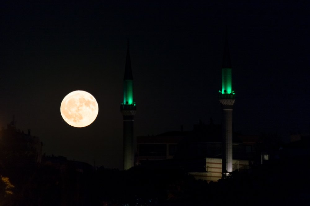 Dramatic full moon rising over at night with mosque silhouette