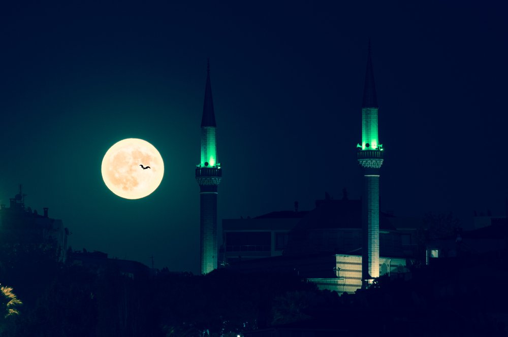 Dramatic full moon rising over at night with mosque silhouette