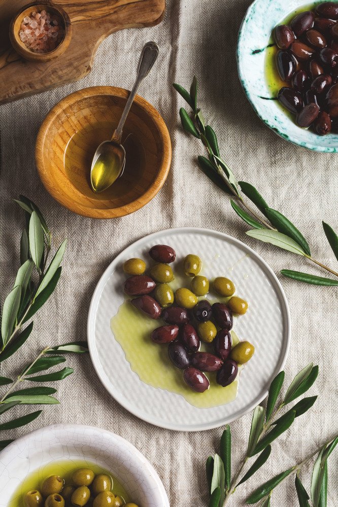 Black olives and olives in oil decorated with fresh branches of an olive tree on a table and napkins from old linen.