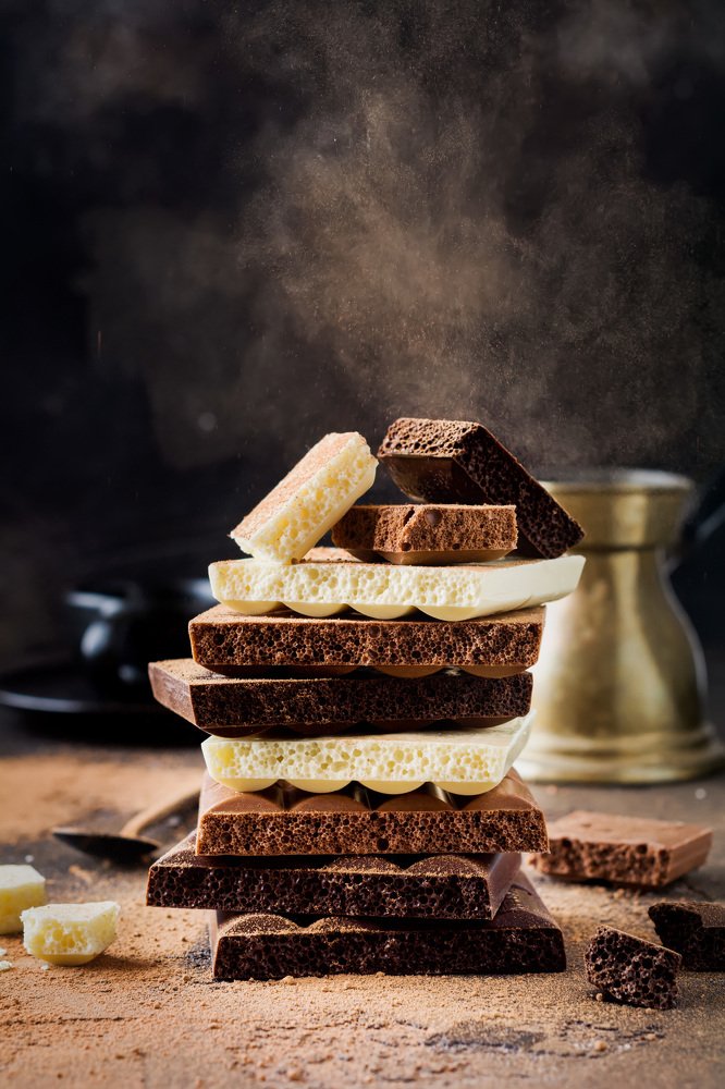 Stack of various chocolate, white, bitter and milk in a cloud of cocoa powder on an old table