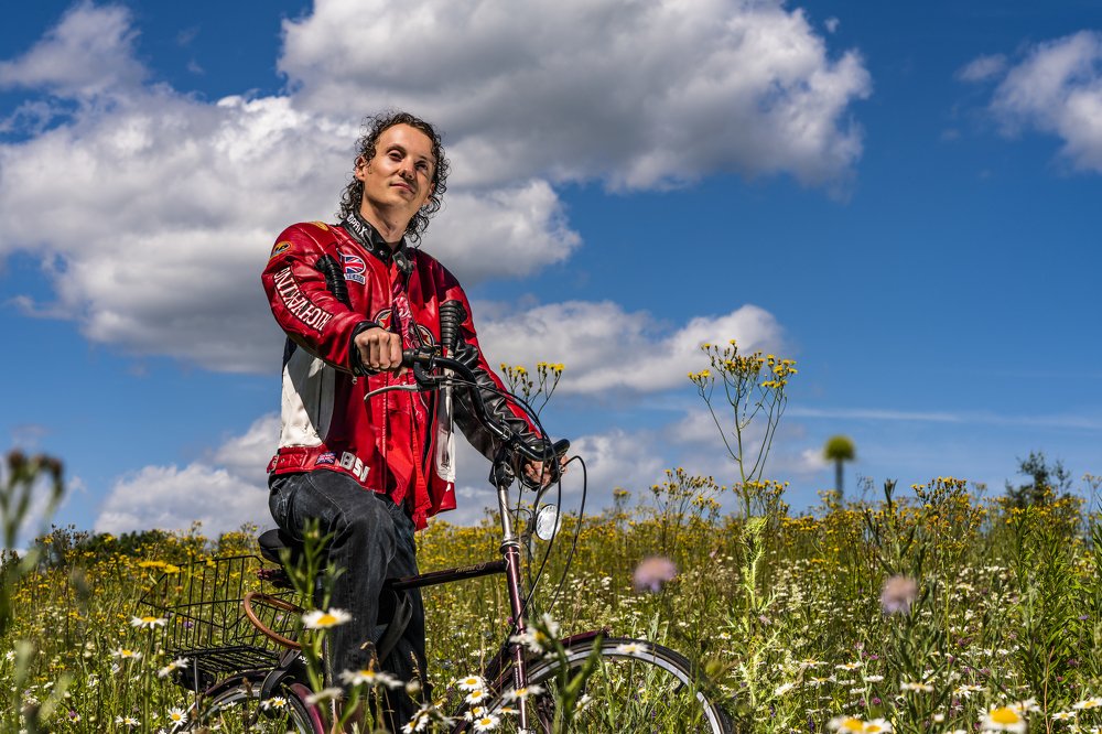 A young man in a field of flowers on a Bicycle under the clouds