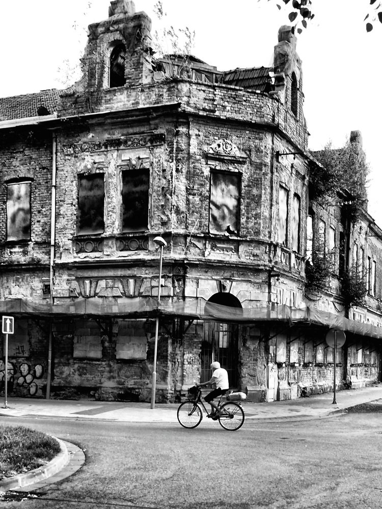 Woman cycling in front of a dilapidated hotel