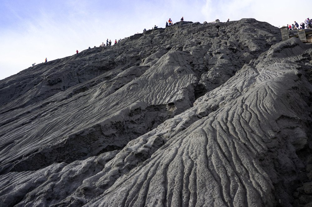 Люди на склоне вулкана среди потоков застывшей лавы.