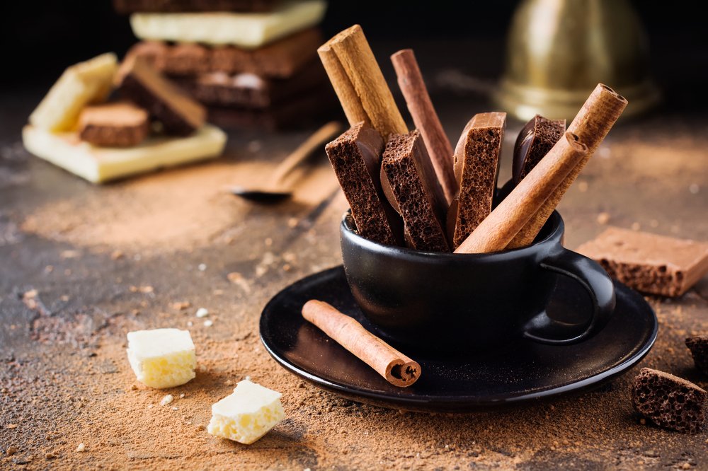 Pieces of porous chocolate and cinnamon sticks in black coffee cup.