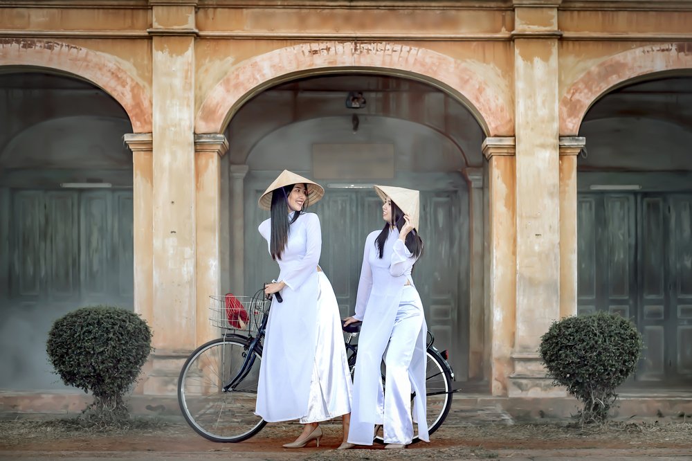 Two beautiful women in Vietnam\'s national costume Riding a bicycle to see ancient buildings.