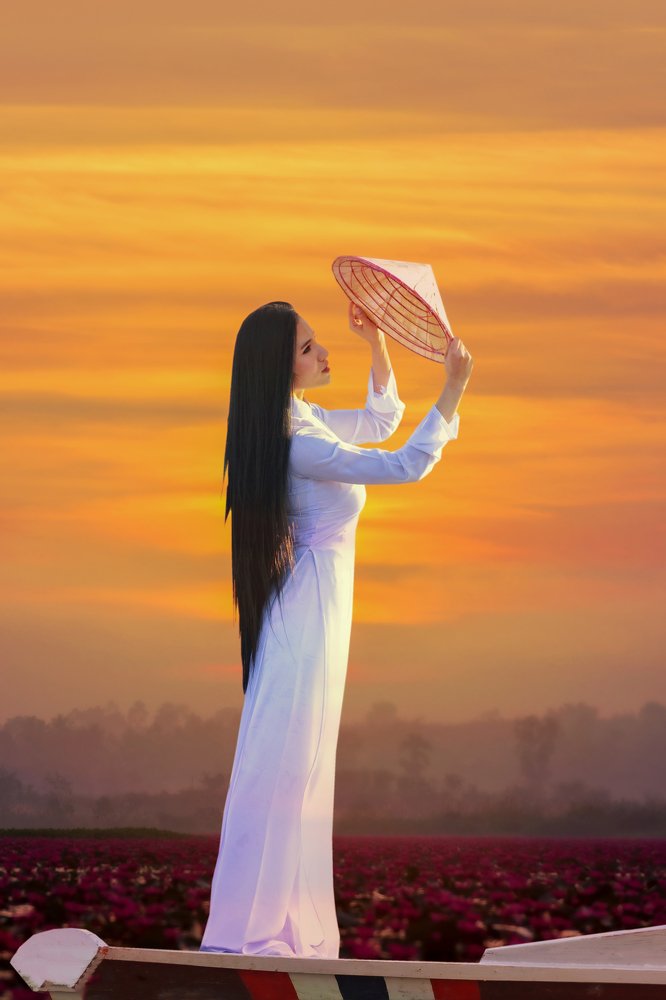 Beautiful woman in traditional Vietnam national costume Standing with her hat on the bow of the lotus pond at sunrise