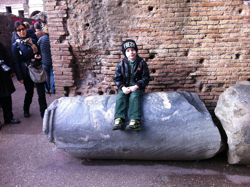 Сын сидит на куске колонны Рим колизей.