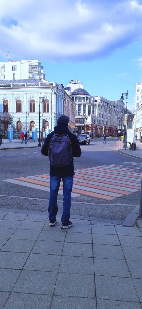 Москва. Молодой человек с рюкзаком собирается перейти дорогу.