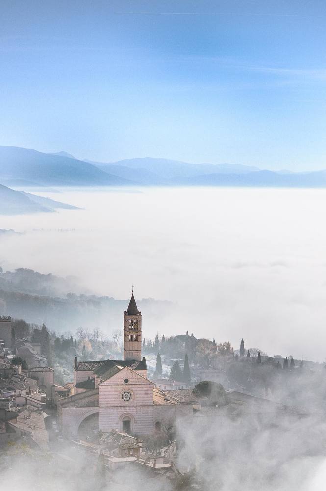 Базилика Святой Клары в итальянском городе Ассизи в облаке осеннего тумана на рассвете