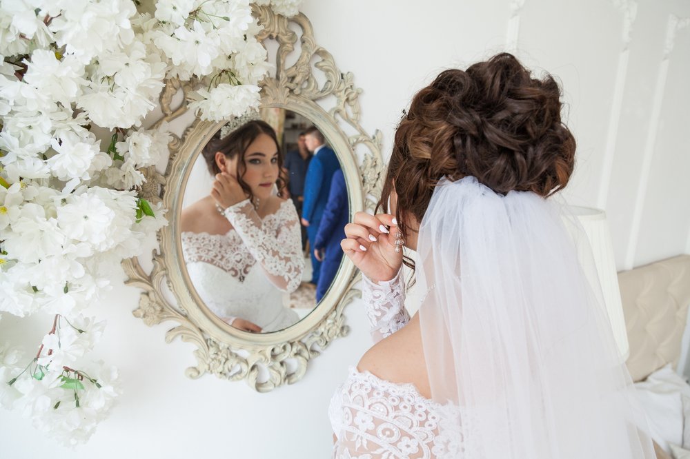 Невеста перед зеркалом поправляет серьги